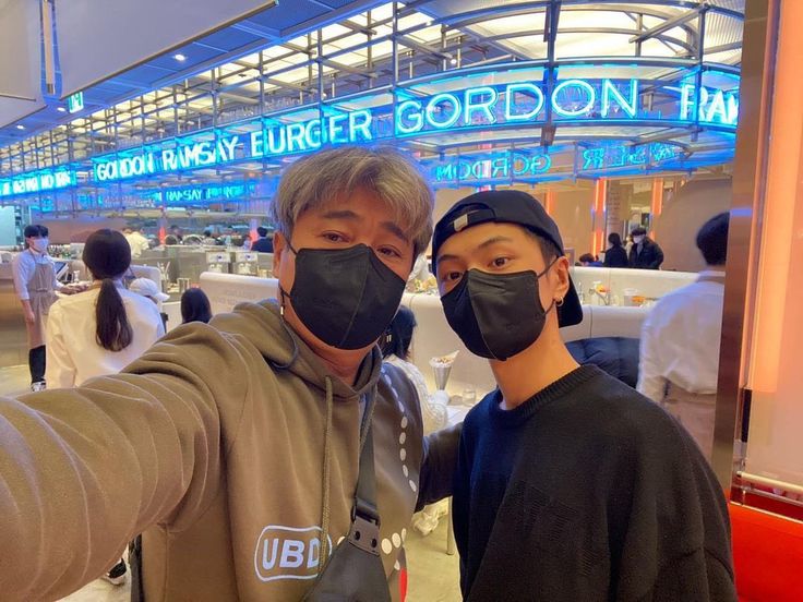 two people wearing face masks taking a selfie in an airport terminal, one person is pointing at the camera