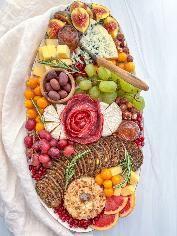 a platter filled with different types of cheeses and fruit on top of a white cloth