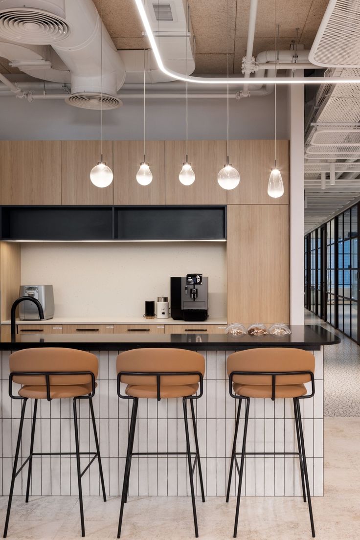 three bar stools sit in front of an island with four lights hanging from the ceiling