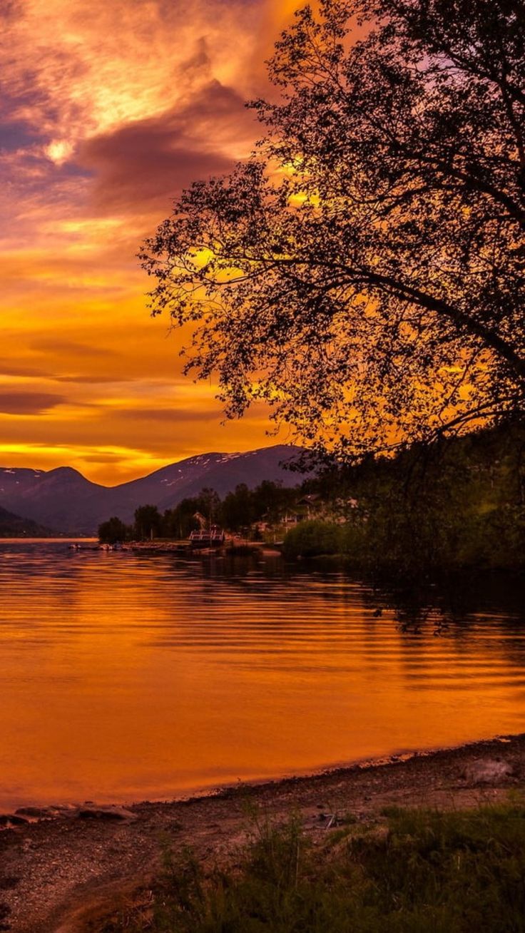 an orange and yellow sunset over a lake with mountains in the backgrouund