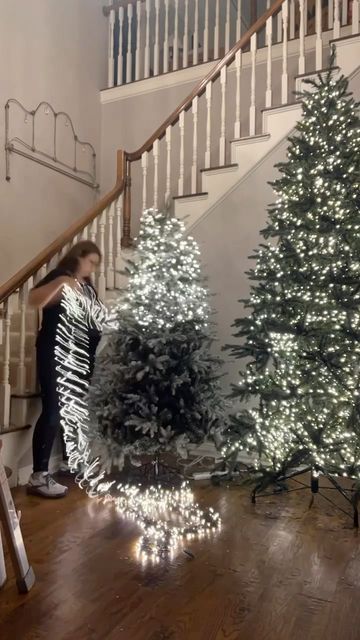 two christmas trees on the ground in front of a stair case with lights all around them