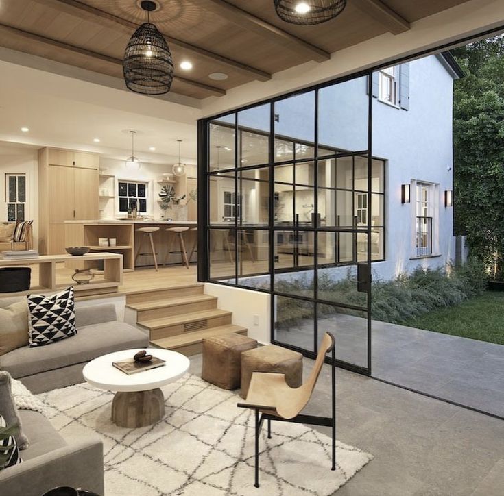 a living room filled with furniture and lots of windows next to a staircase leading up to a kitchen