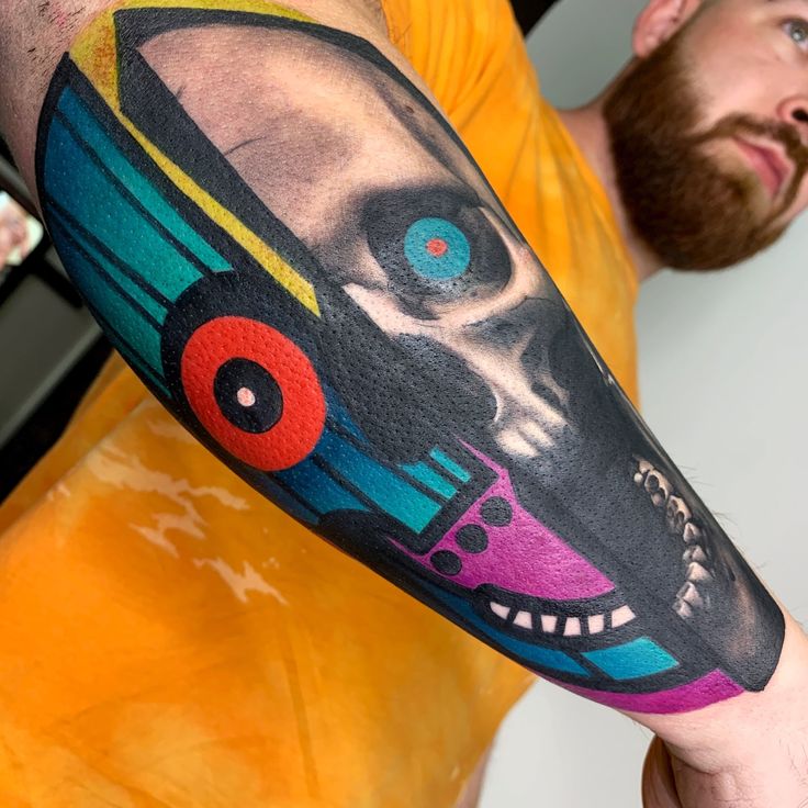 a man with a colorful skull and train tattoo on his arm, next to a yellow t - shirt