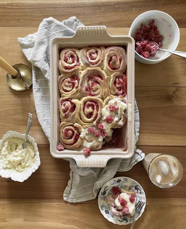 a pan filled with food on top of a wooden table next to bowls and spoons