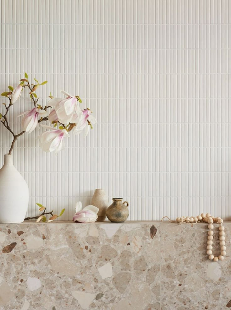 a white vase with flowers and beads on a shelf in front of a wallpapered background