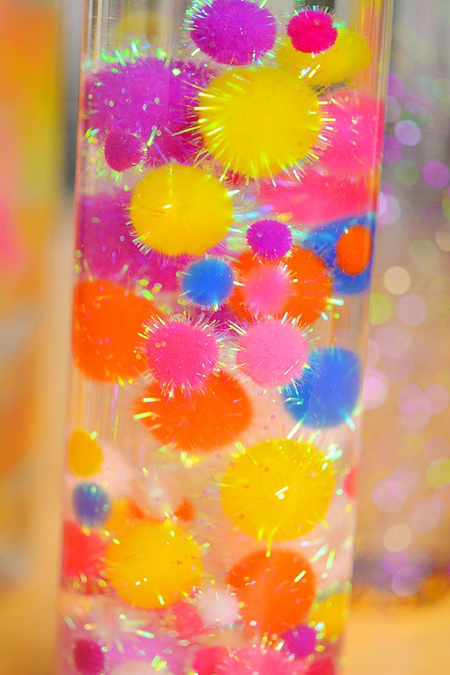 a glass filled with lots of different colored pom - poms on top of a table