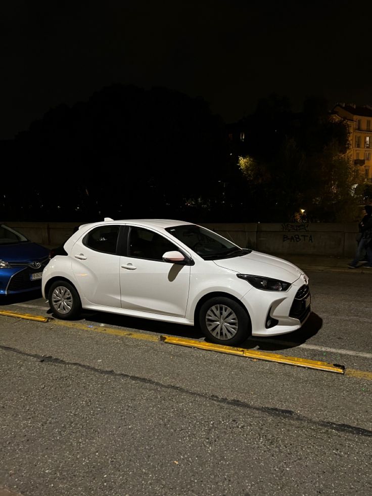 two cars are parked on the side of the road at night, one is white and the other is blue