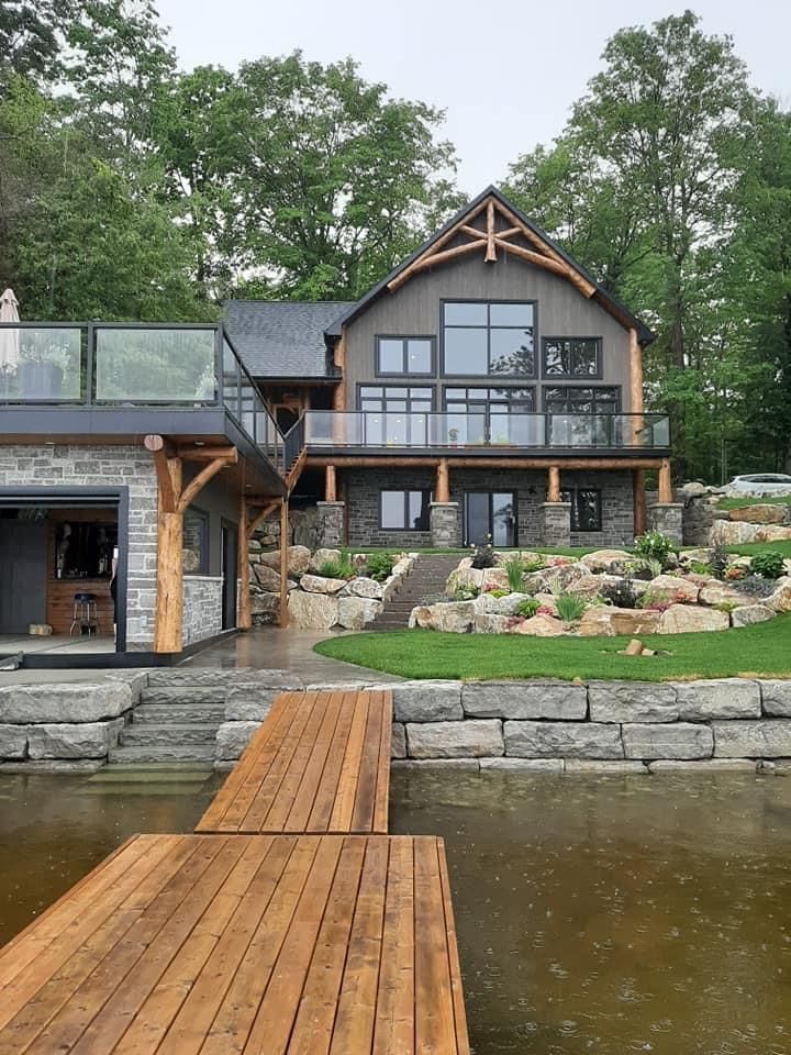 a large house sitting on top of a lake next to a wooden dock in front of a lush green forest