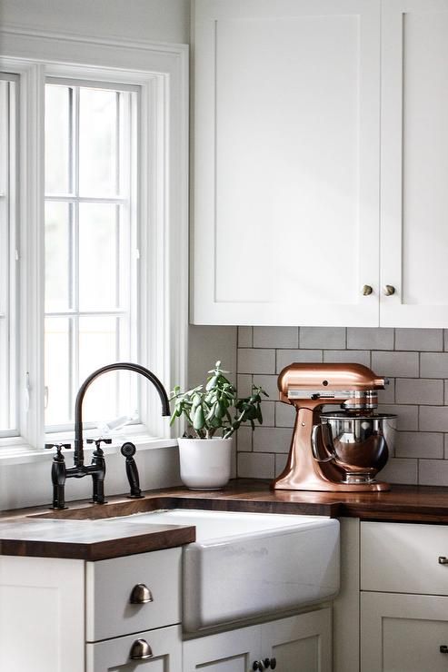 a kitchen with white cabinets and brown counter tops, an old mixer on the sink