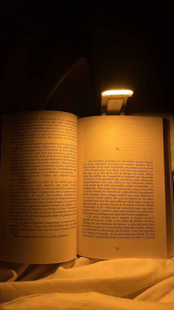 an open book sitting on top of a bed next to a night light in the dark