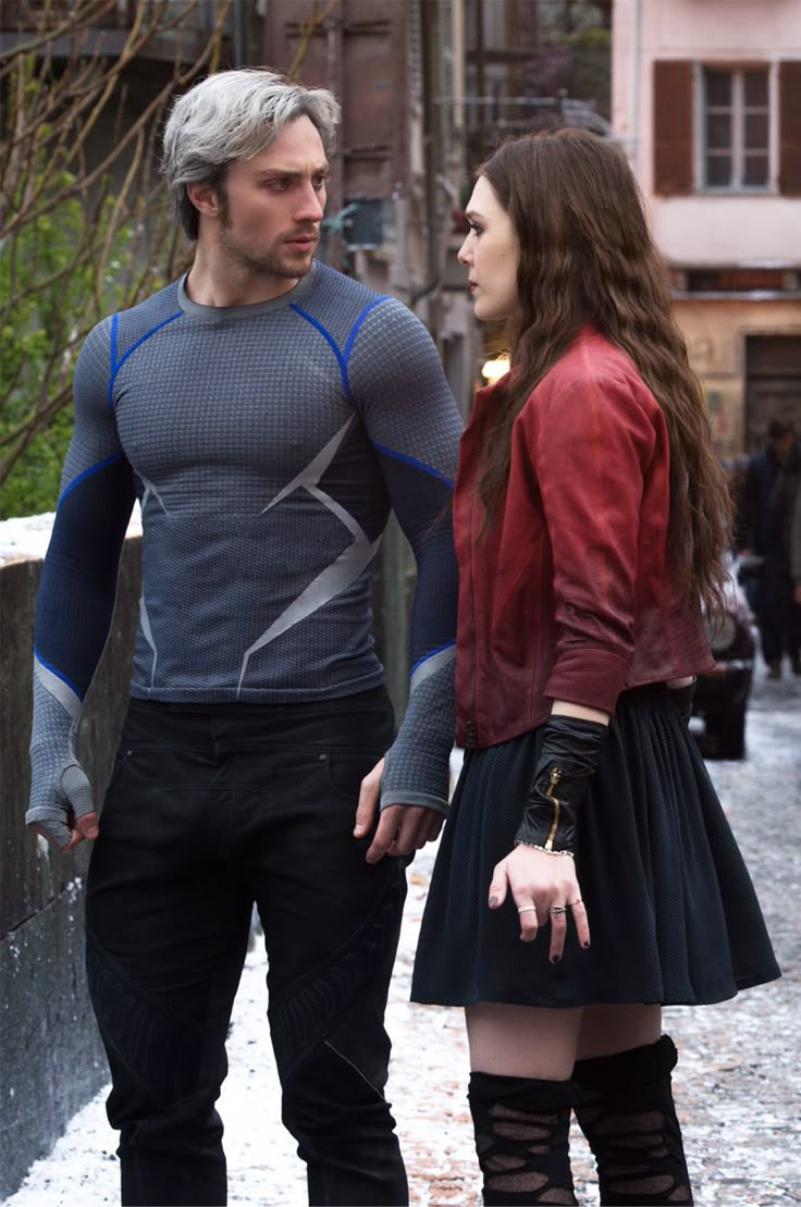 a man and woman standing next to each other on a street with buildings in the background