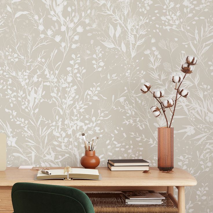 a desk with a book, vase and flowers on it in front of a wall