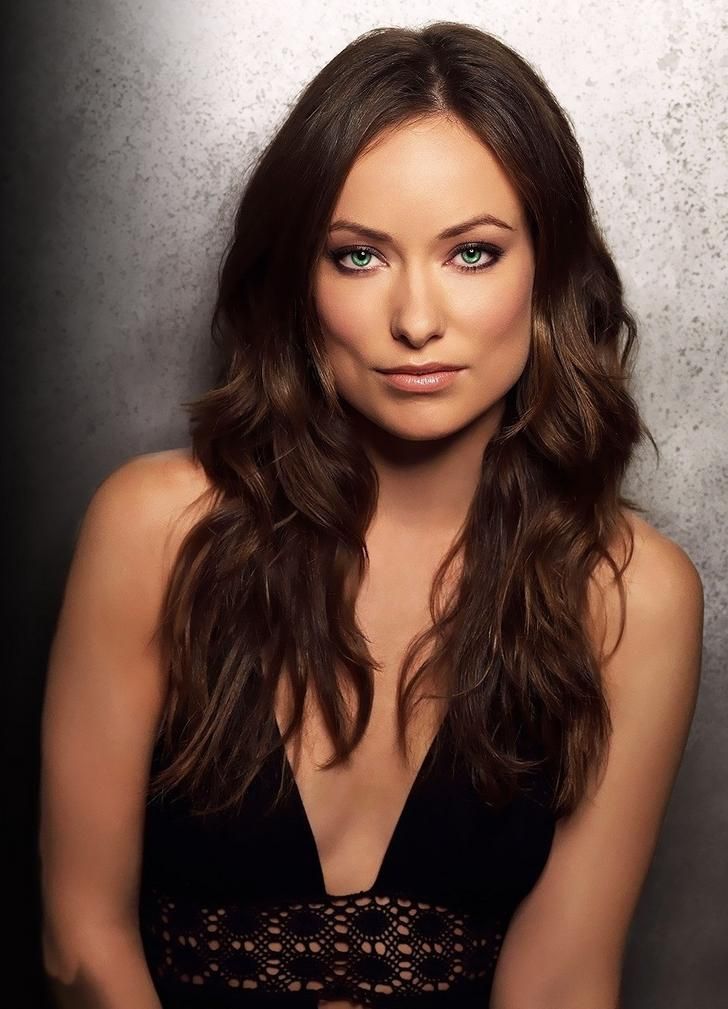 a woman with long hair and blue eyes posing for a photo in front of a wall