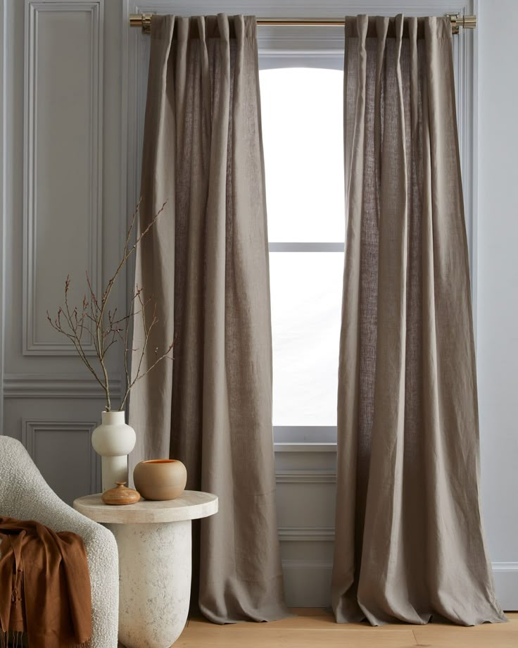 a chair and table in front of a window with drapes on the windowsill