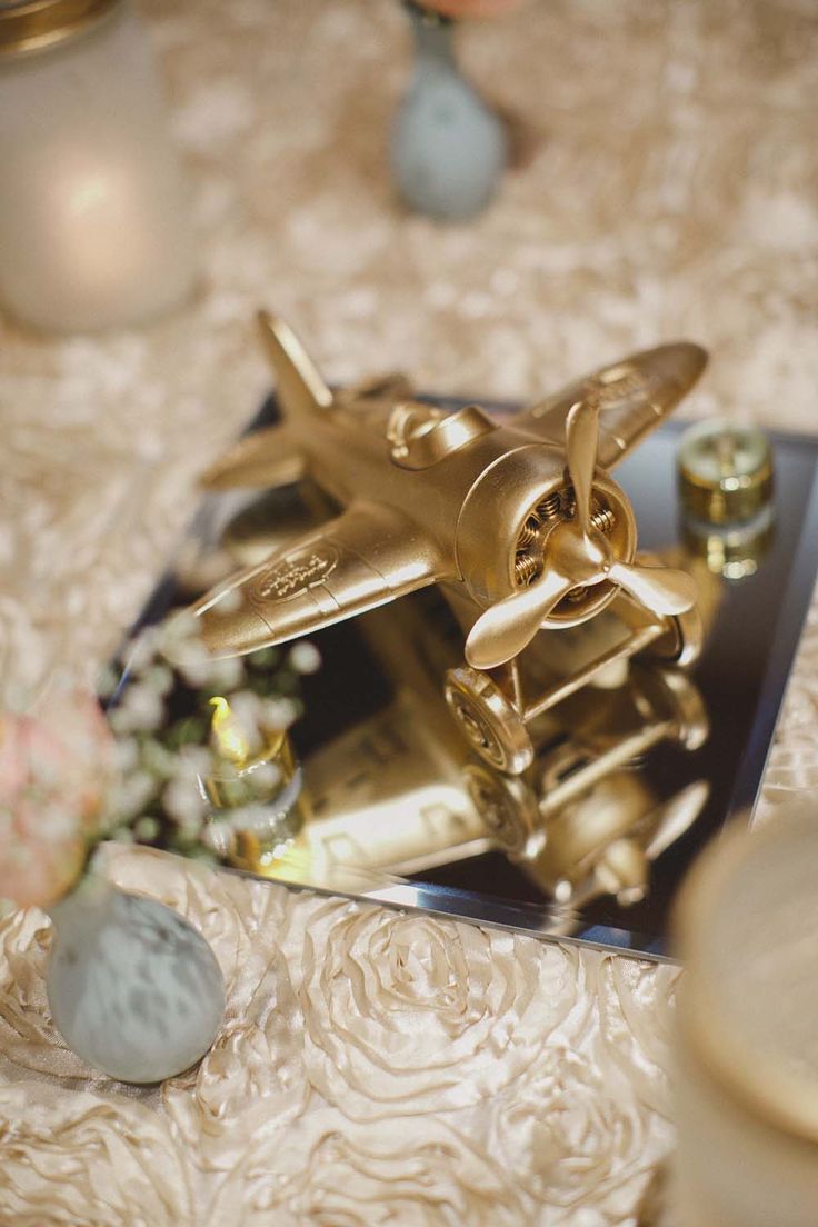 a gold model airplane sitting on top of a table next to some rocks and flowers