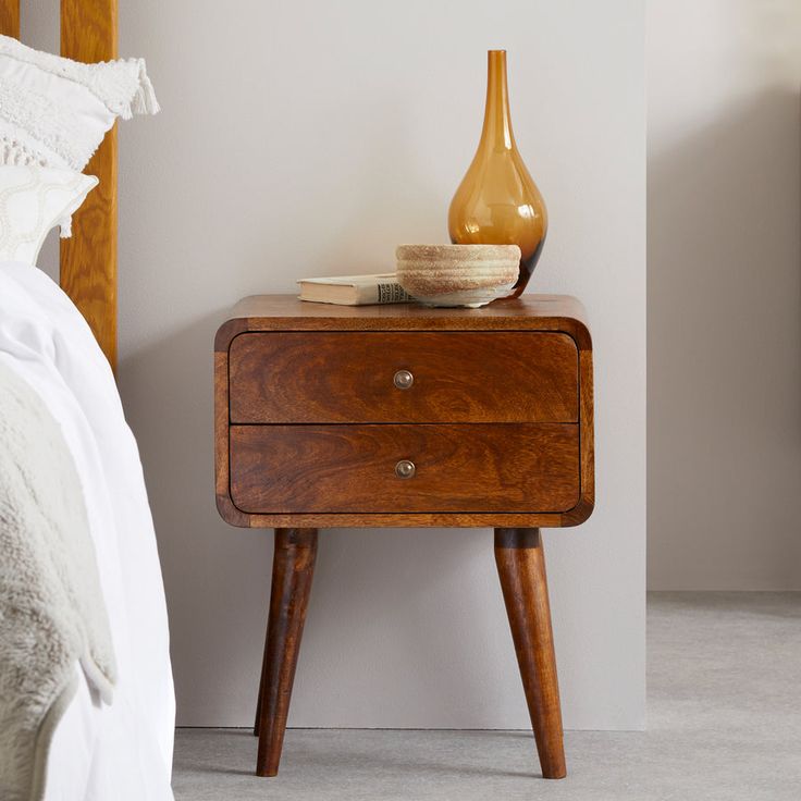 a nightstand with a vase on it next to a bed