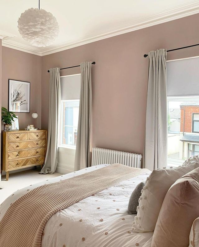 a bedroom with pink walls and white bedding, beige curtains on the windowsill