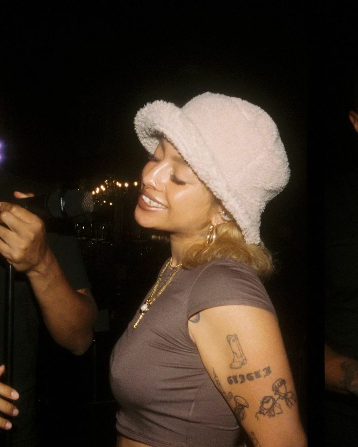 a woman wearing a white hat and holding a microphone in front of a man with tattoos on his arm