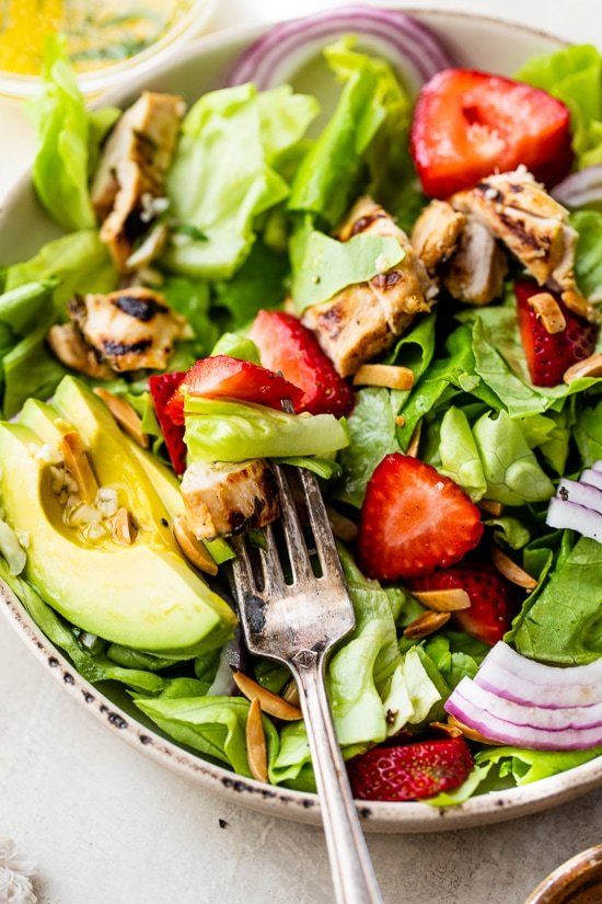 a salad with strawberries, avocado and chicken on it is ready to be eaten