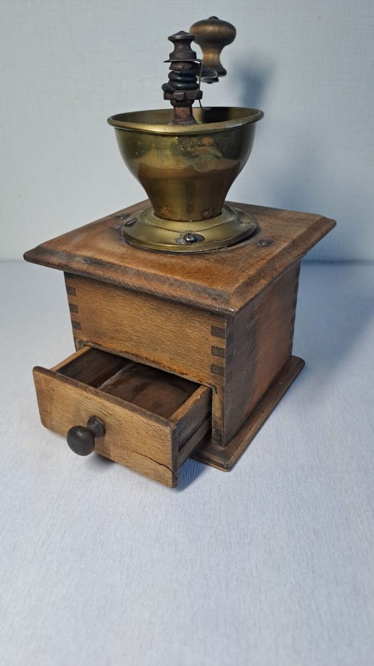 an old wooden box with a brass bowl on top and drawers below it, sitting on a white surface