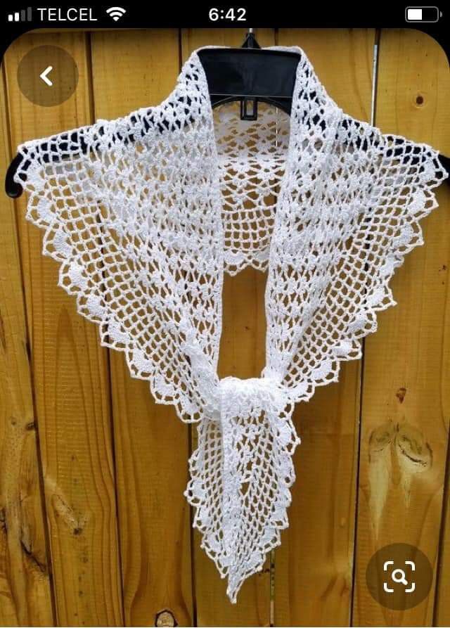 a white crocheted shawl hanging on a wooden wall with a hook in it