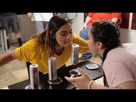 two women sitting at a table with cans of soda in front of them, talking