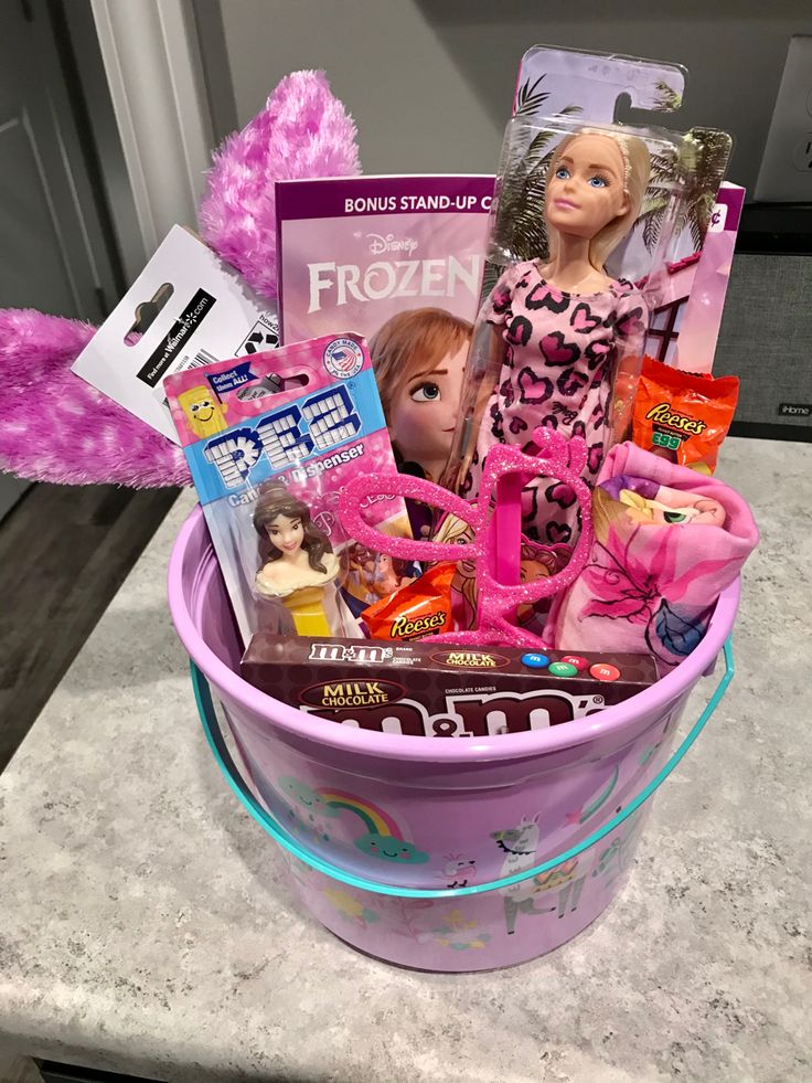 a pink bucket filled with barbie dolls and other toys on top of a counter next to a stuffed animal