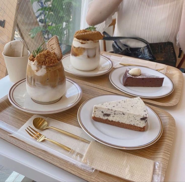 three desserts on plates sitting on a table with goldware and utensils