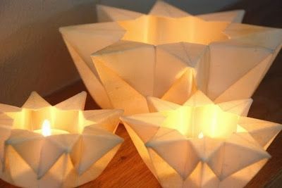 three white candles sitting on top of a wooden table next to paper cups with lights in them