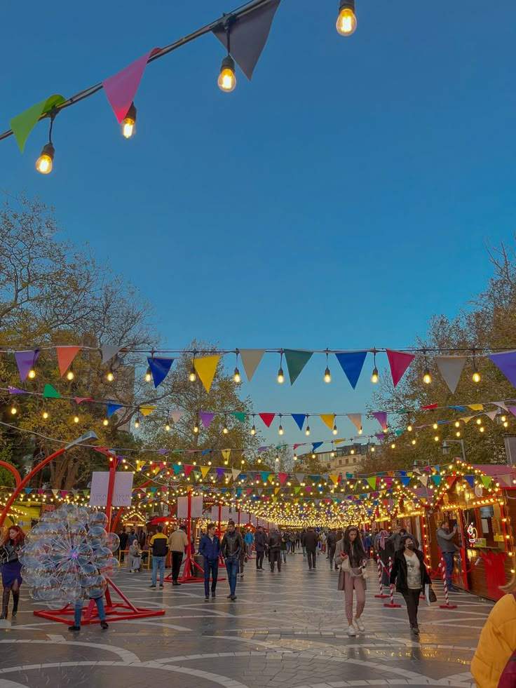 many people are walking around in an open area with lights and decorations on the ceiling