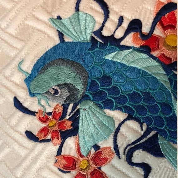 a blue bird with flowers on it's back is embroidered onto the side of a quilt