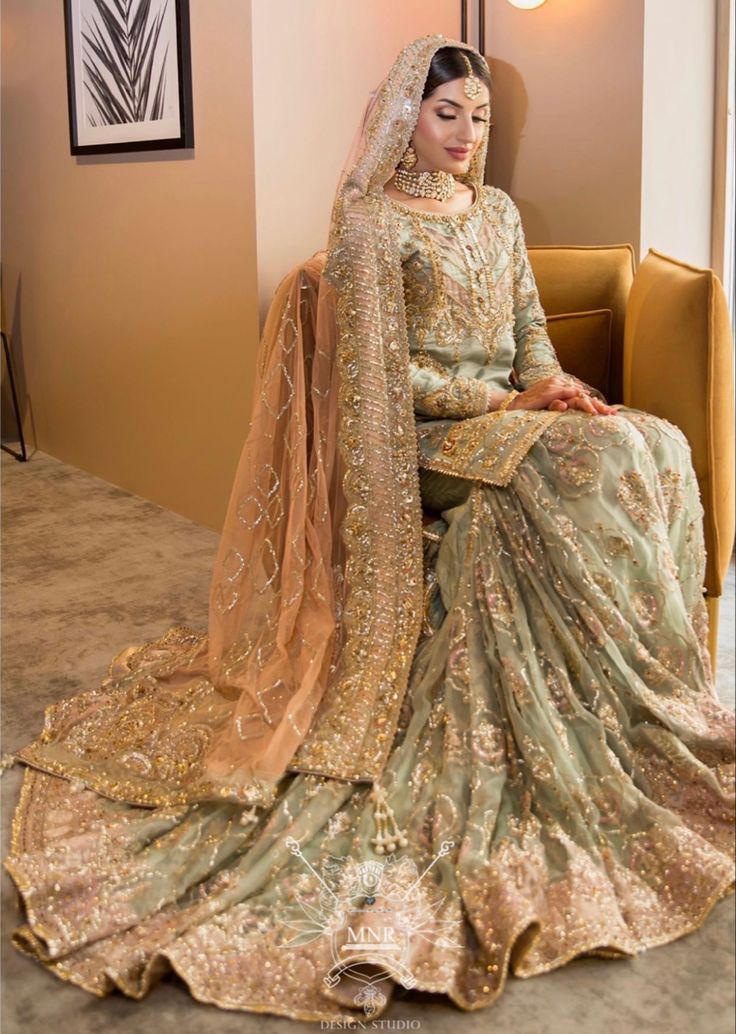 a woman sitting on top of a couch wearing a green and gold wedding dress with long veil