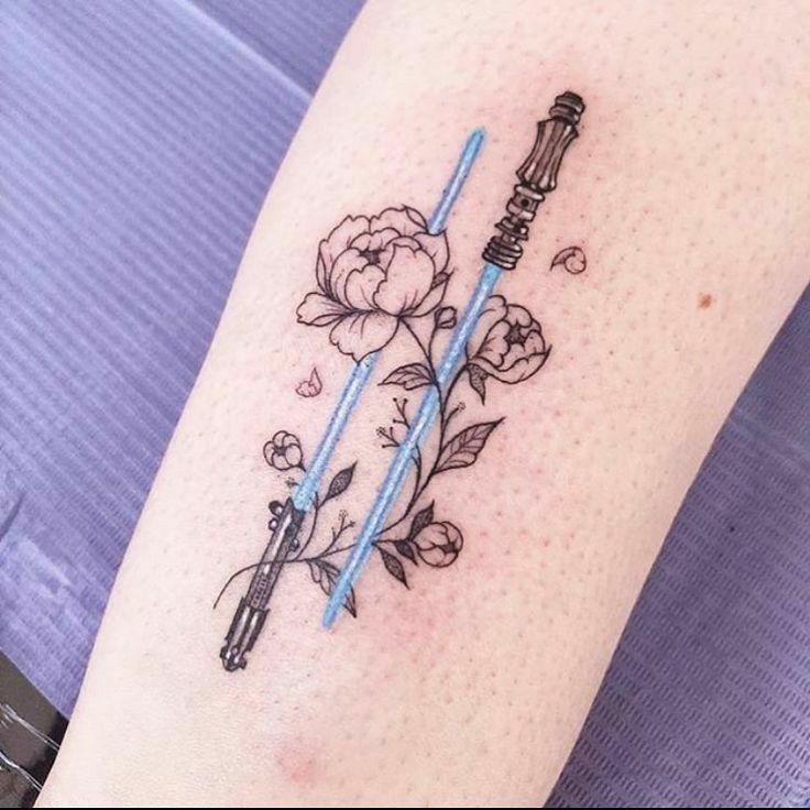 a star wars tattoo with two lightsabes and flowers on the arm, one is blue