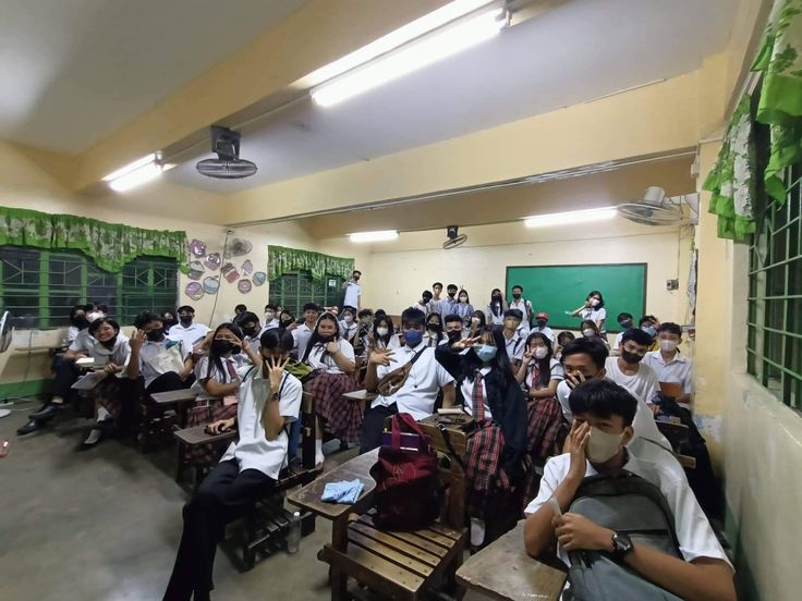 a classroom full of students wearing masks and sitting on desks in front of them