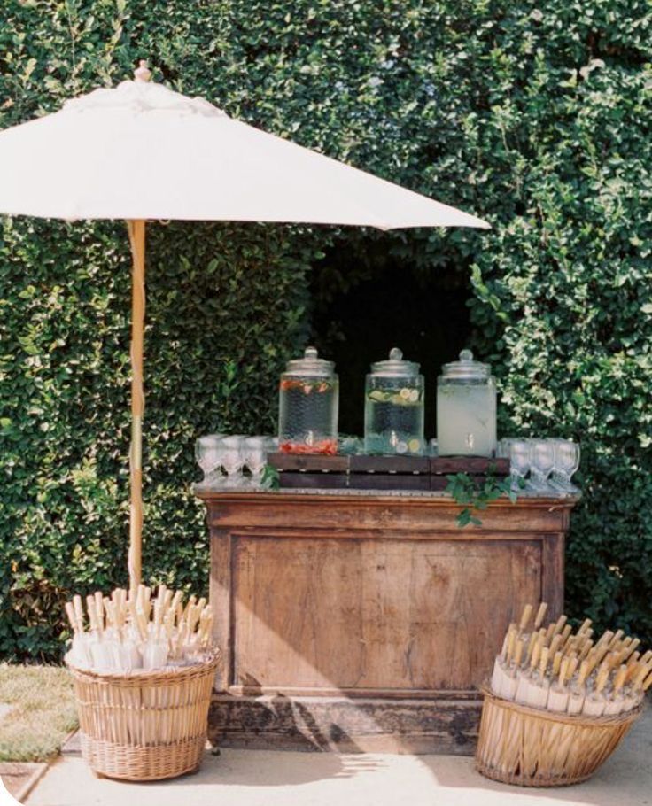 an umbrella and some drinks in baskets on the side of a road with bushes behind it