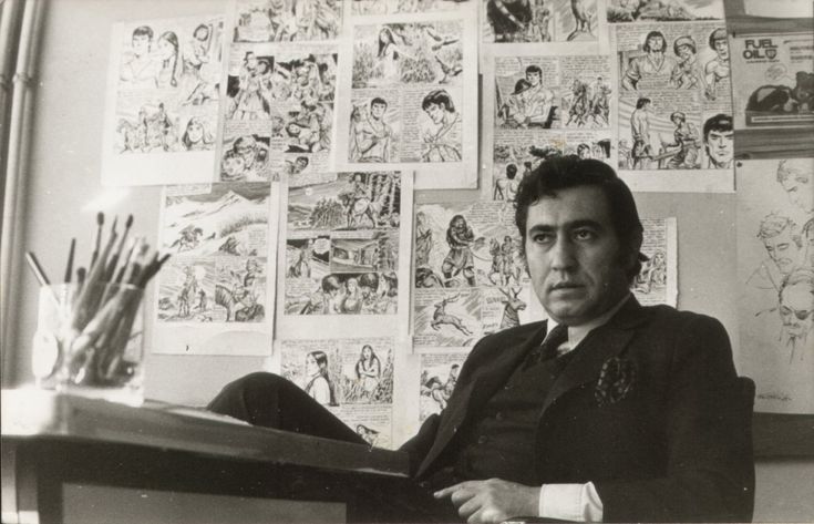 a man sitting in front of a desk with lots of comics on the wall