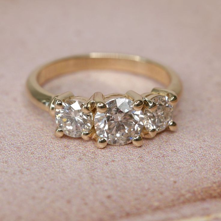 three stone diamond ring sitting on top of a pink cloth covered table with gold trim