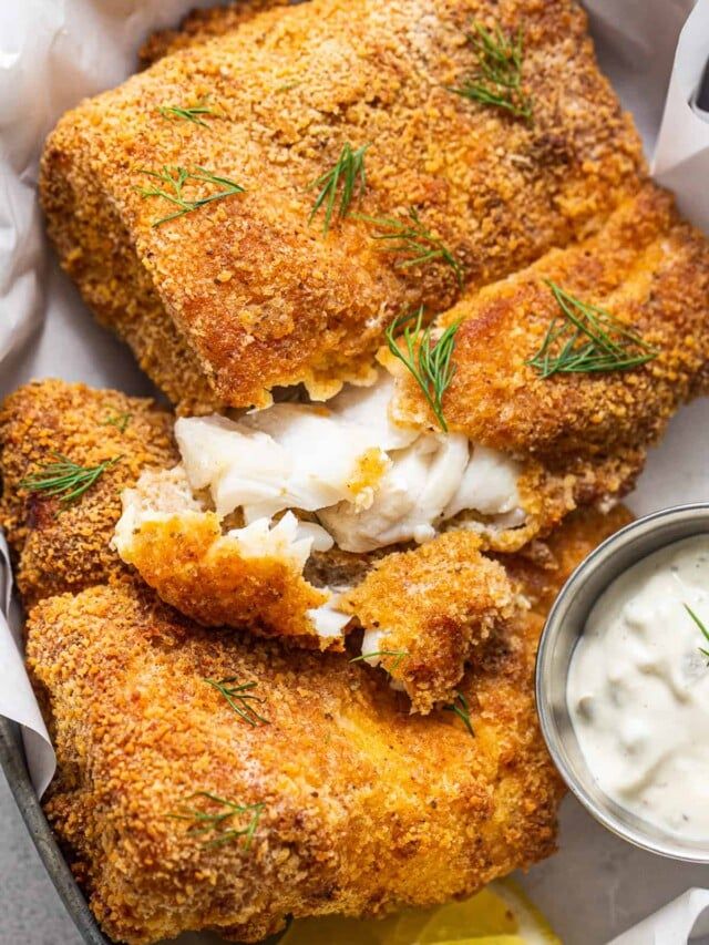 two fried fish fillets in a basket with lemon wedges and sour cream sauce