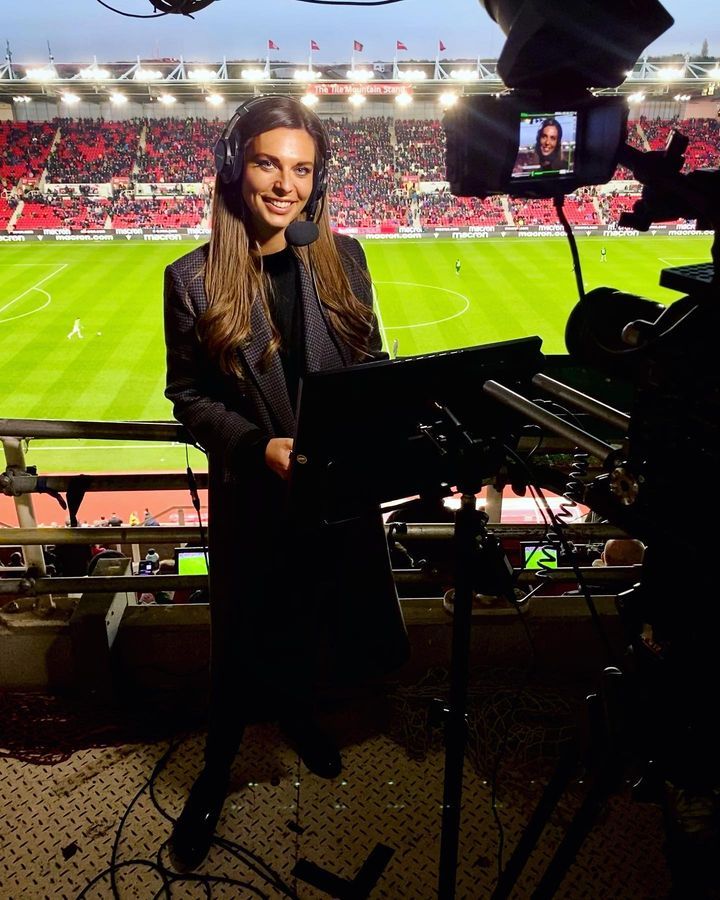 a woman standing in front of a camera on top of a soccer field