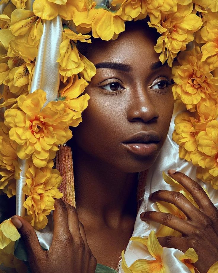 a woman with yellow flowers on her head and hands in front of her face, posing for the camera