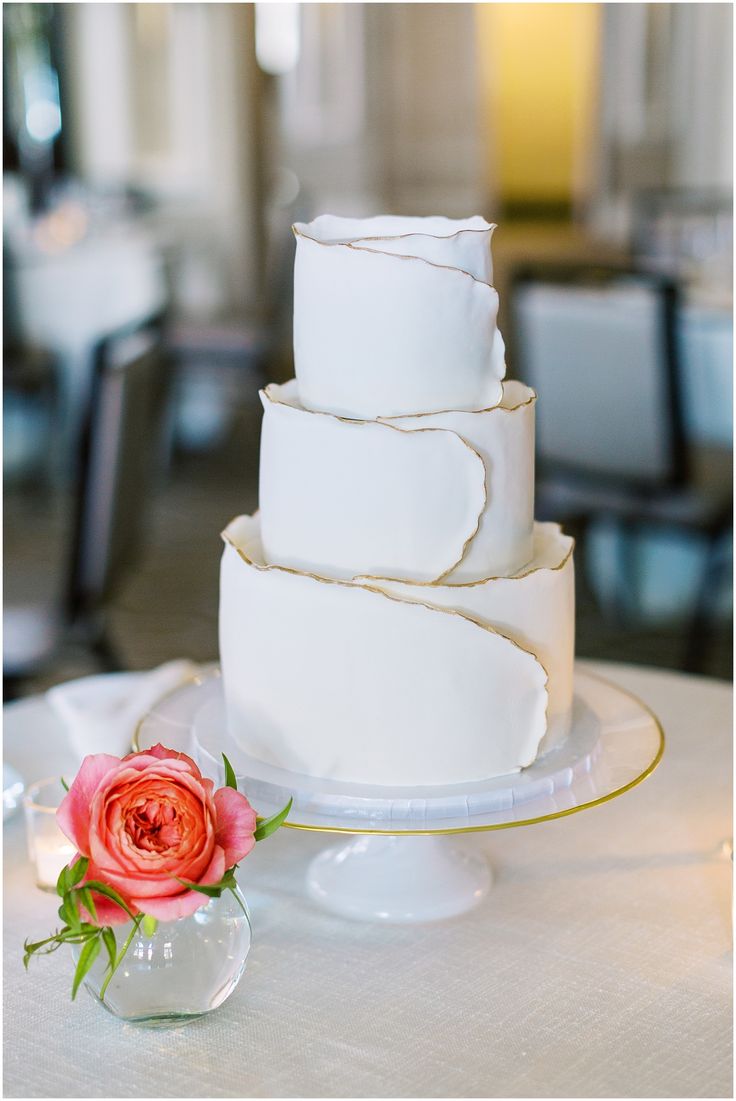 a three tiered white cake sitting on top of a table next to a pink flower