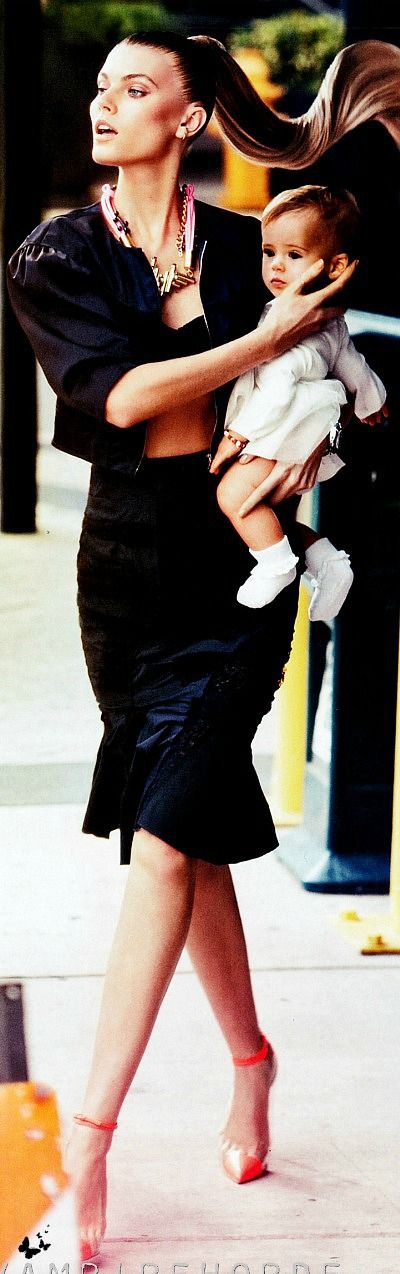 a woman holding a baby in her arms while walking down the street with other people