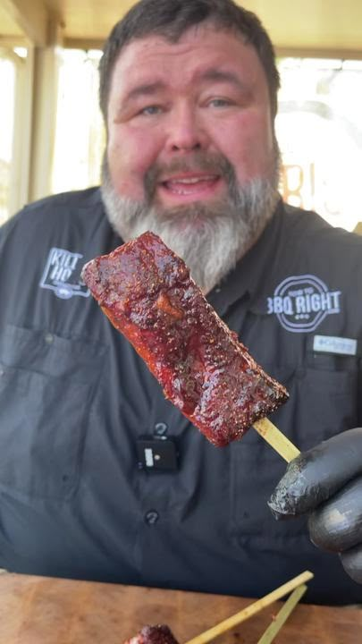 a man with a beard is holding up a piece of meat and toothpicks