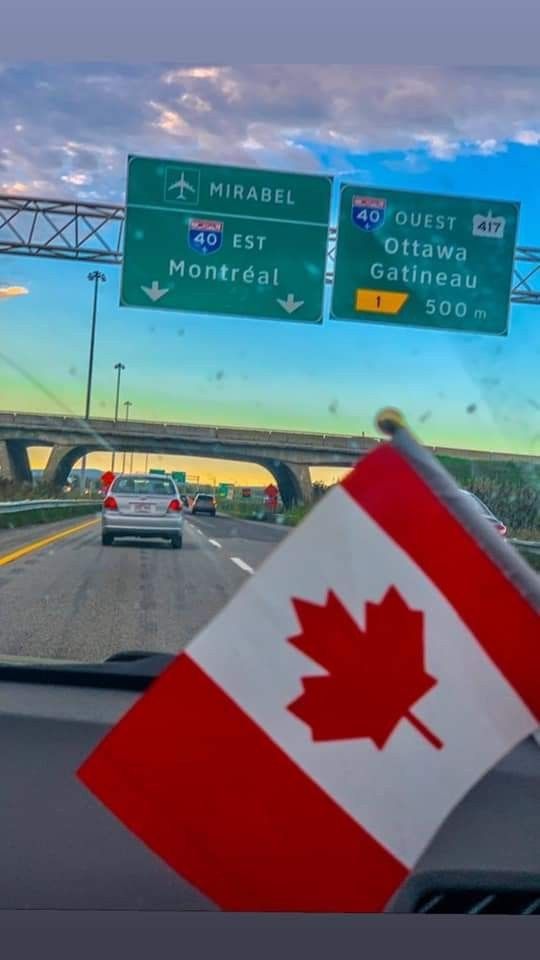 the canadian flag is waving in front of an overpass with highway signs above it