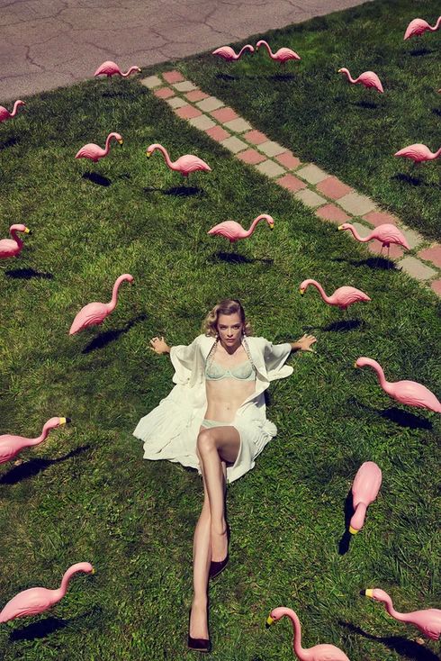 a woman laying in the grass surrounded by pink flamingos, with her legs spread out