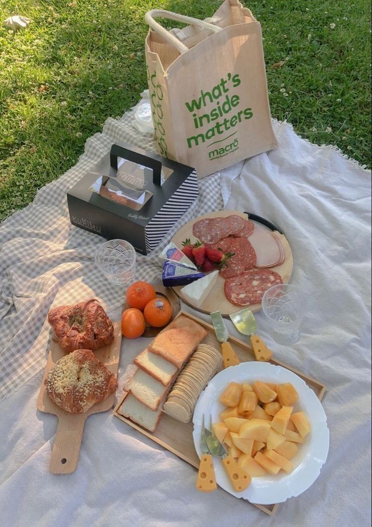 an assortment of cheeses and meats on a picnic blanket with a tote bag