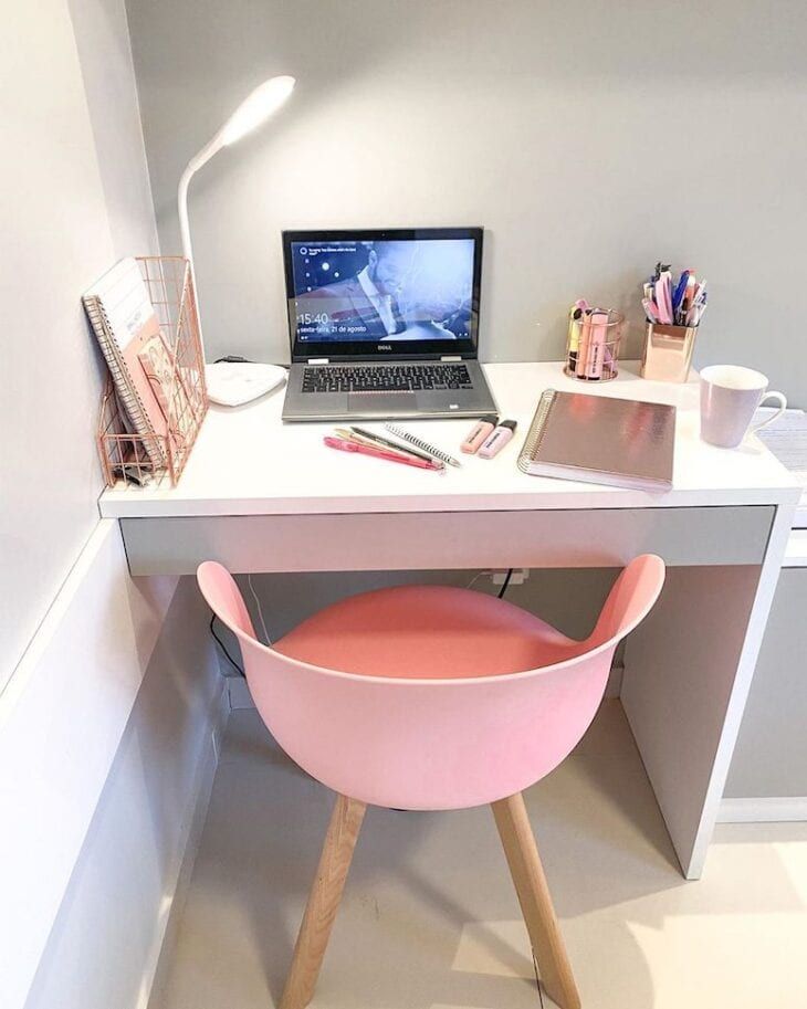 a laptop computer sitting on top of a desk next to a pink chair and lamp