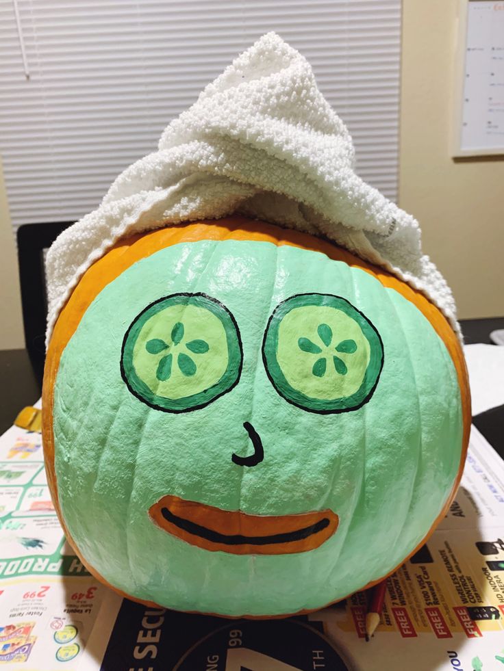 Medium sized pumpkin with green face mask and cucumber eyes, topped with a wrapped towel covering the stem. Halloween Pumkin Ideas Paint, Pumpkin Face Mask Paint, Self Care Pumpkin Painting, Yellow Painted Pumpkin Ideas, Facial Pumpkin Painting, Pumpkins Painting Ideas Cute, Avocado Pumpkin Painting, Cool Halloween Pumpkin Painting Ideas, Fun Carved Pumpkins