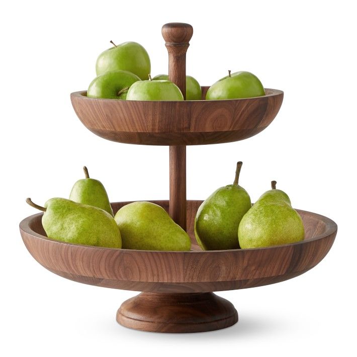 three tiered wooden bowl with apples and pears on the bottom, in front of a white background