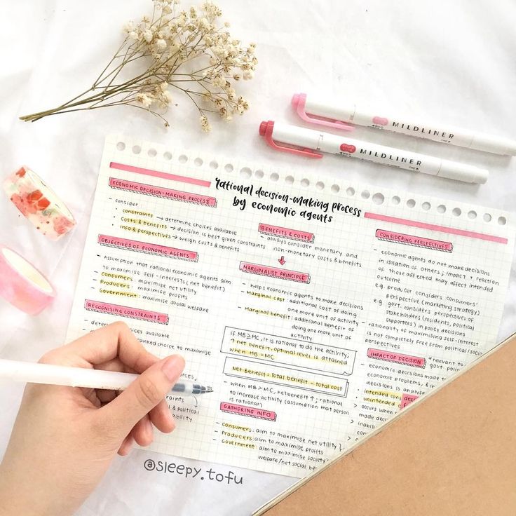 a person is writing on a piece of paper next to some flowers and pencils